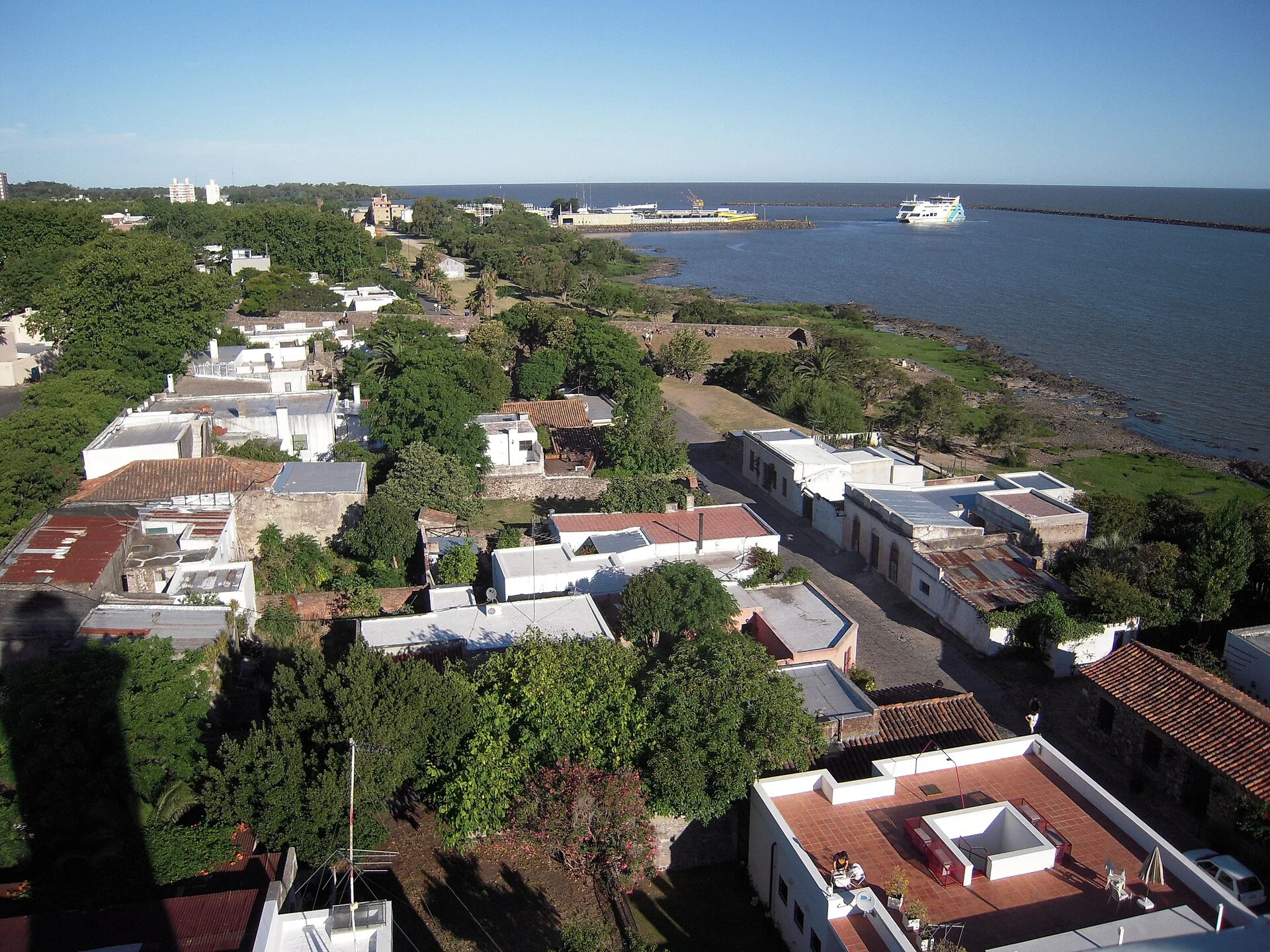 Vista ampla de Colônia do Sacramento e do porto de ferry, observada à distância a partir do farol, sob luz natural.