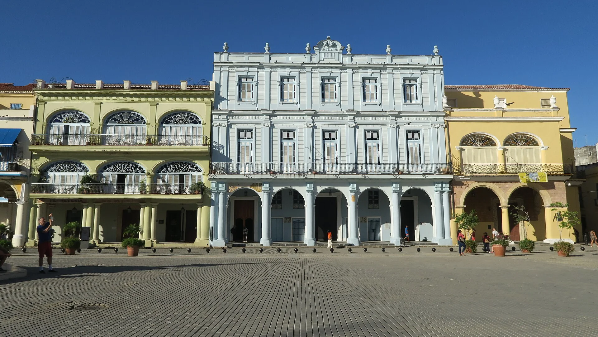 Fachadas históricas em tons pastel e arcadas na Plaza Vieja, em Habana Vieja, sob céu azul.