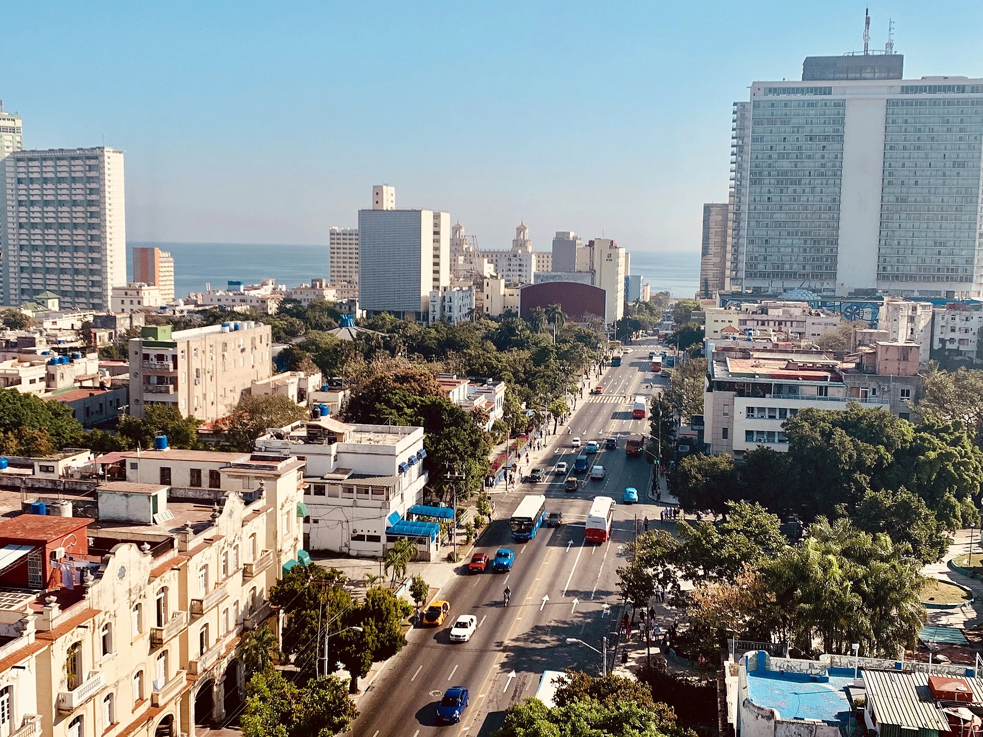 Vista elevada da Avenida 23, La Rampa, no Vedado, com prédios, árvores e o mar de Havana ao fundo.