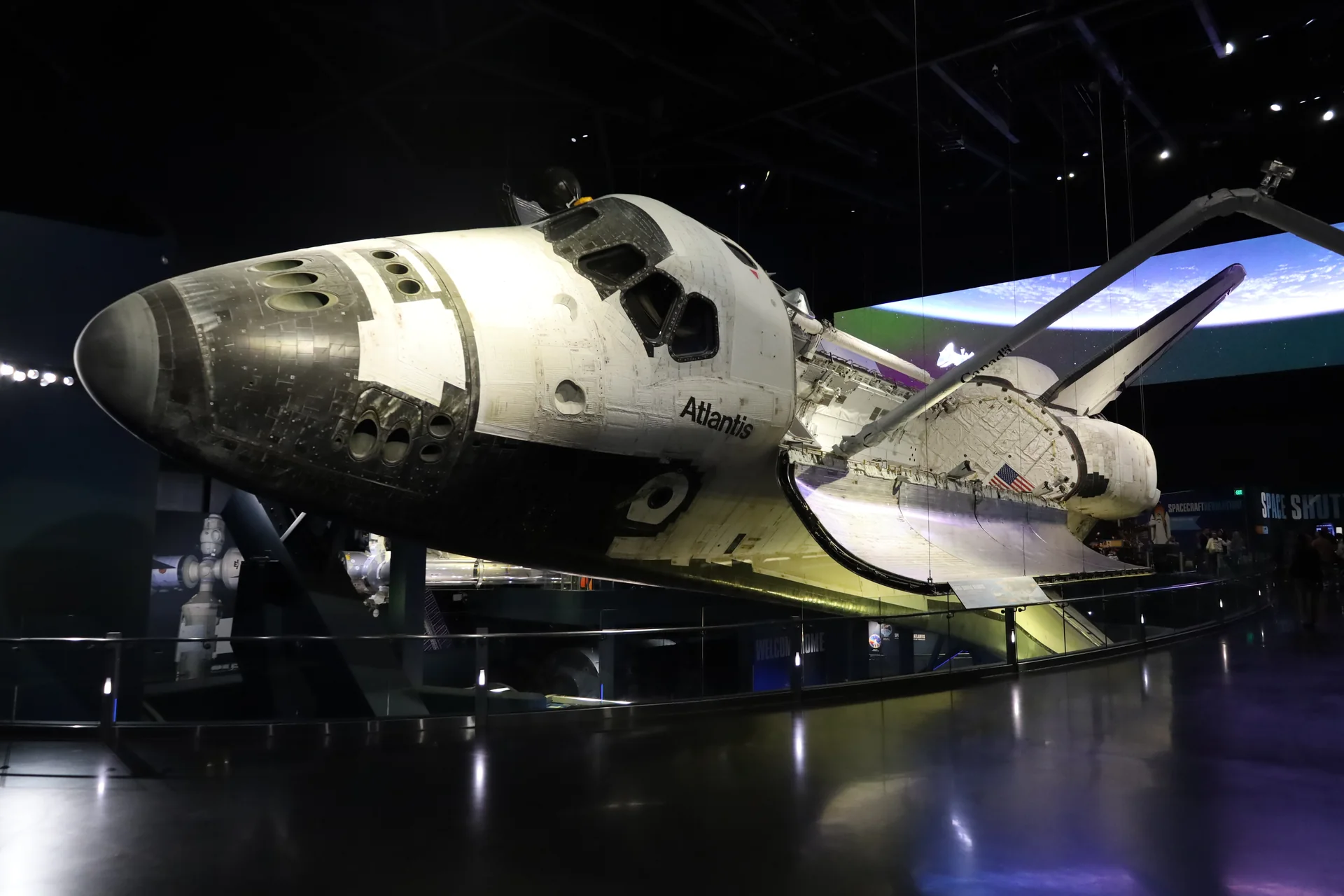 Ônibus espacial Atlantis em exposição no pavilhão do Kennedy Space Center, visto de frente e de lado sob iluminação interna.