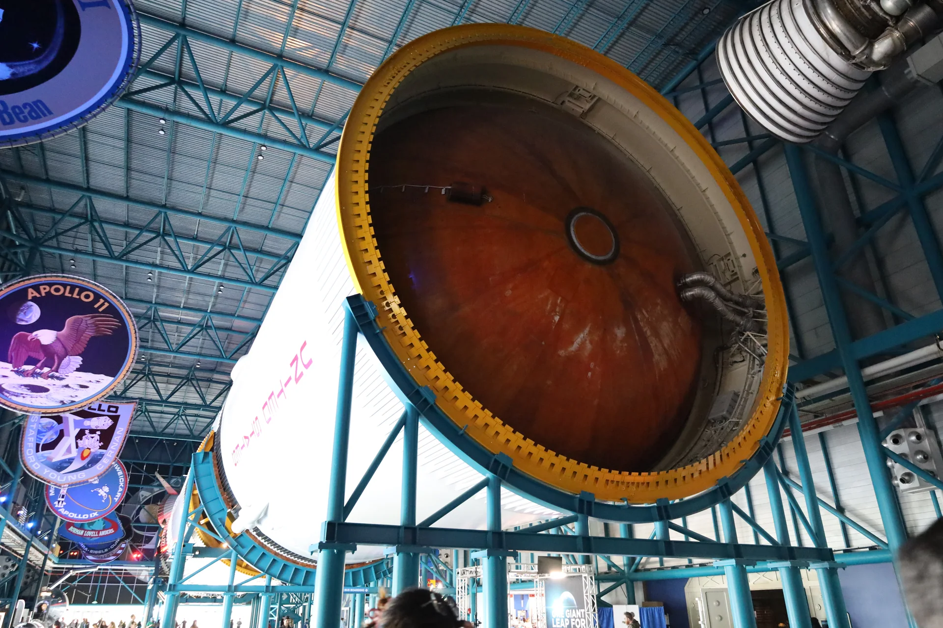 Parte traseira de um foguete Saturn V exposto no Apollo/Saturn V Center, com motores e estrutura do museu ao fundo.