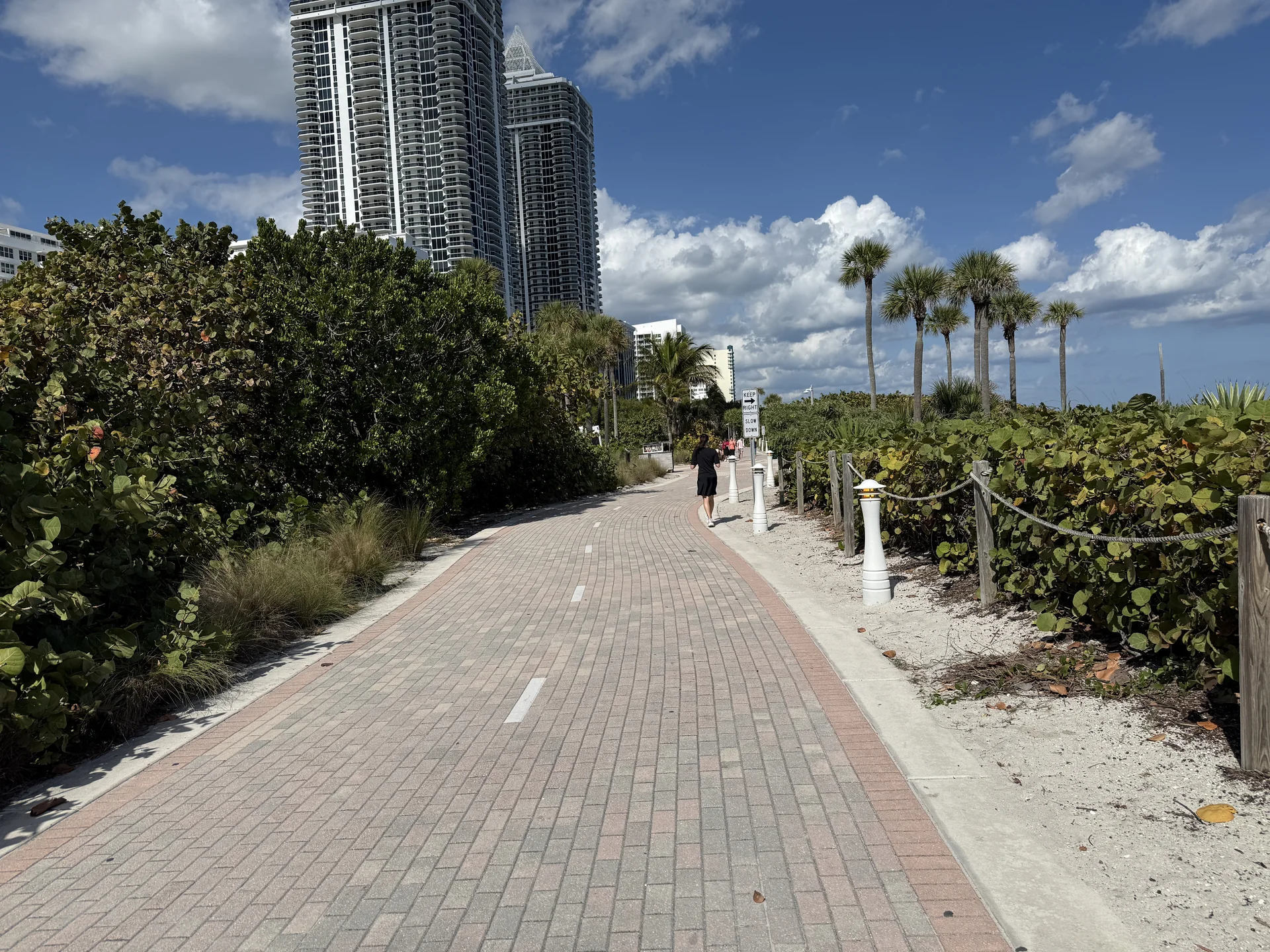 Passeio público à beira-mar em Miami Beach em manhã clara, com pessoas praticando atividade de baixo impacto e oceano ao fundo.