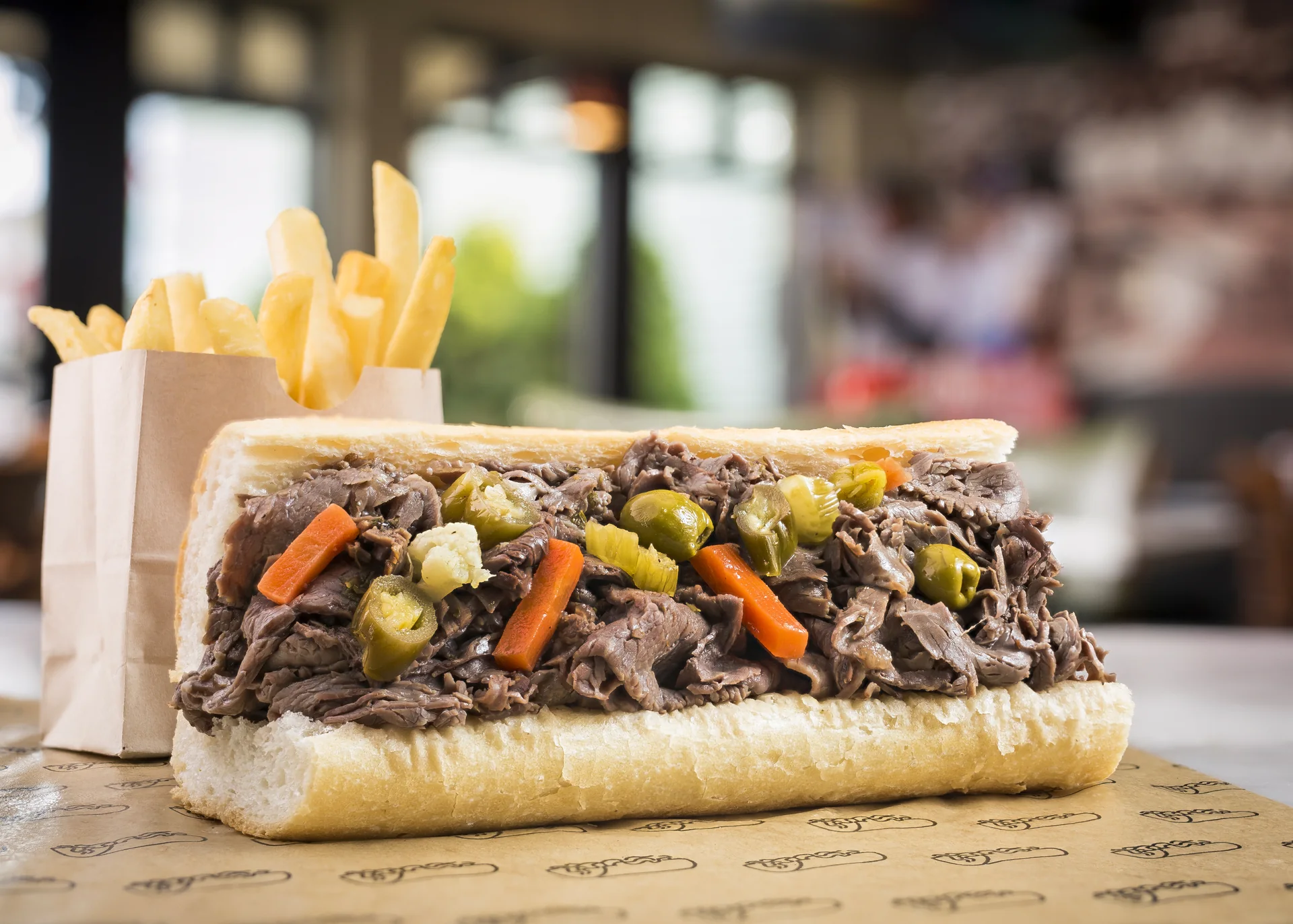 Sanduíche Italian beef aberto, com carne fatiada e giardiniera, sobre balcão.