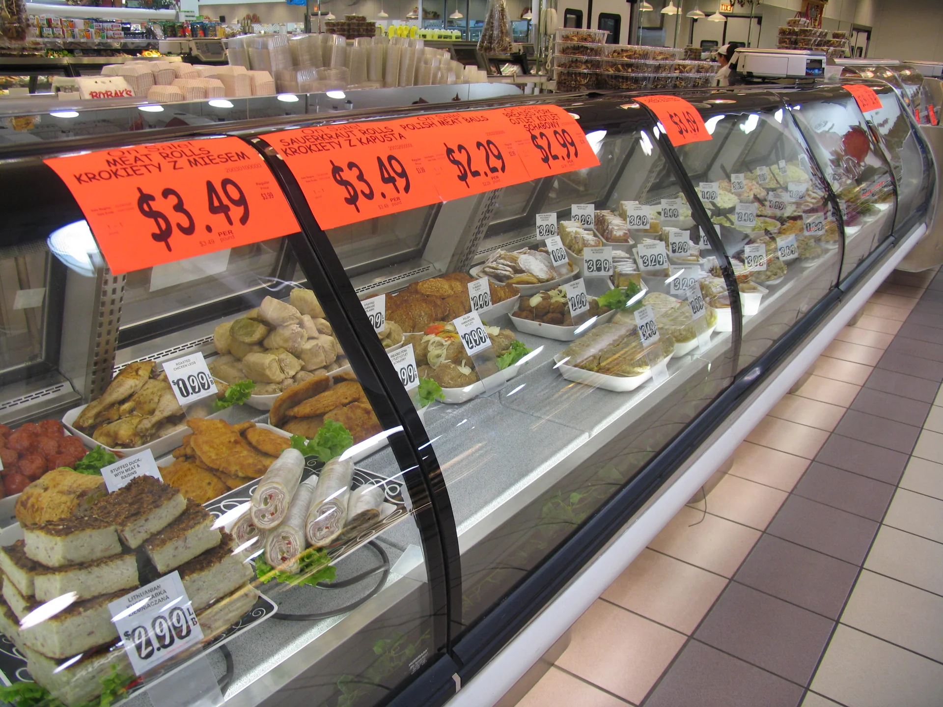 Balcão refrigerado de mercado polonês em Chicago, com pratos preparados e etiquetas de preço.