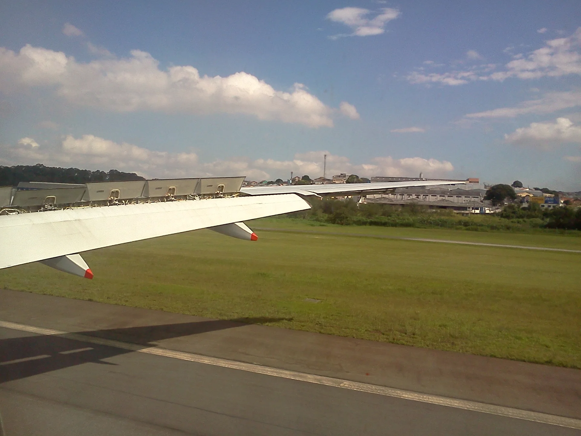 Contexto de mobilidade aeroportuária: asa de aeronave, gramado e céu azul no Aeroporto Internacional de Guarulhos; não representa o parceiro Airport Bus Service.