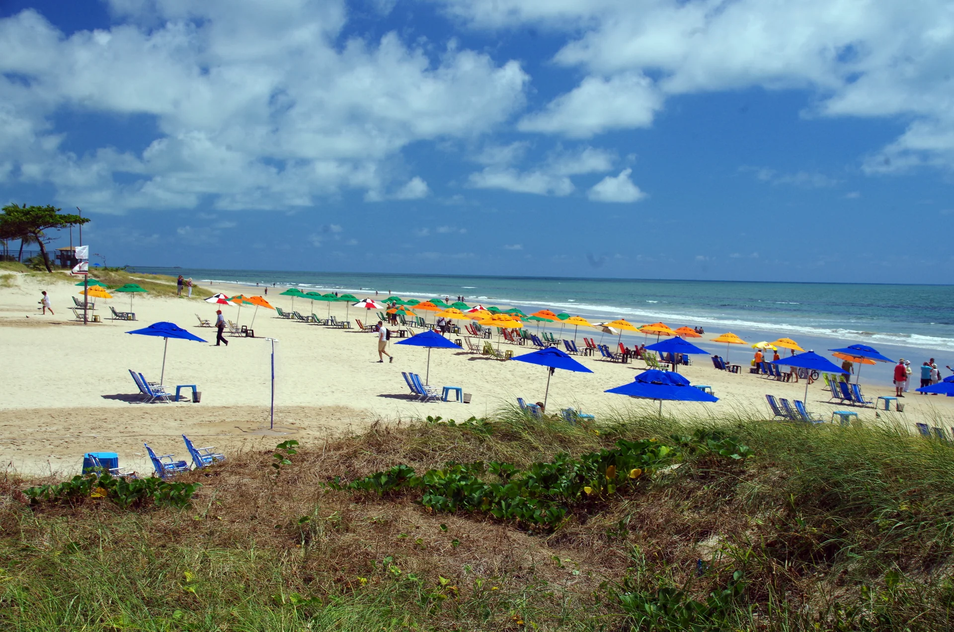 Imagem contextual ensolarada da Praia de Boa Viagem, Recife, com guarda-sóis coloridos; não representa o parceiro Luck Receptivo, a propriedade ou o serviço.