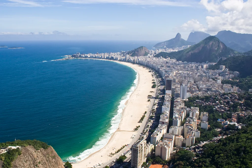 Imagem de contexto de vista aérea ensolarada da Praia de Copacabana e da orla do Rio de Janeiro. Esta imagem é contexto e não representa o parceiro, a propriedade ou o serviço da Orinter Tour & Travel.